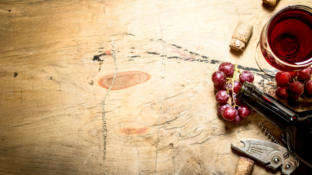 Weinflasche Domaines Les Freres Dubois auf Holztisch mit Glas, Korken und Trauben