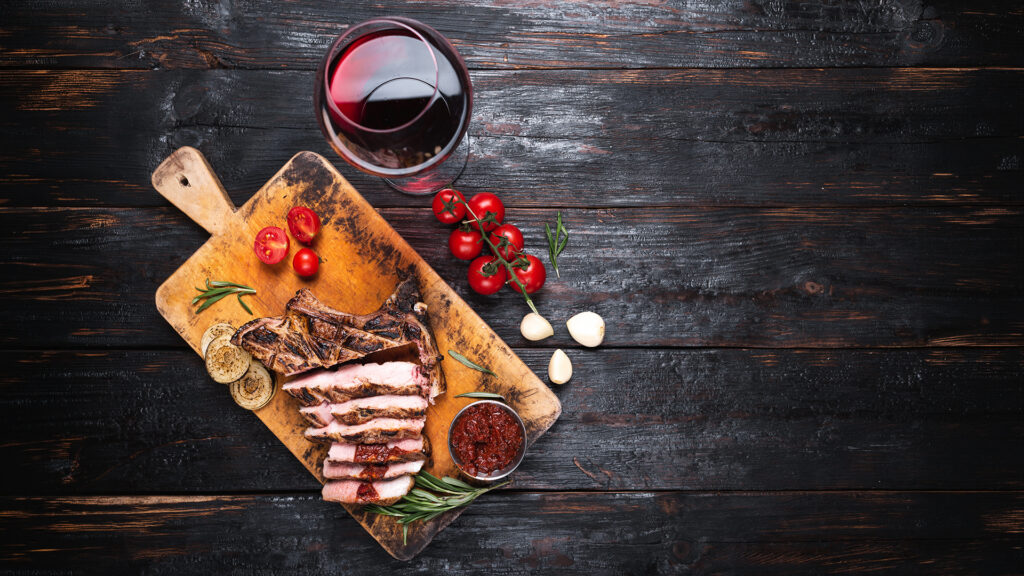 Rotweinglas neben gebratenem Fleisch aus der Weinregion Rhônetal Frankreich