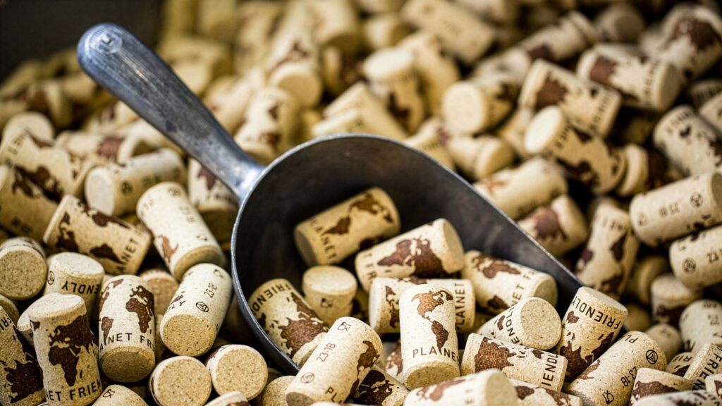 Metallkelle liegt auf einem Haufen Weinkorken mit Weltkarten-Motiv und Texten wie "PLANET FRIENDLY".