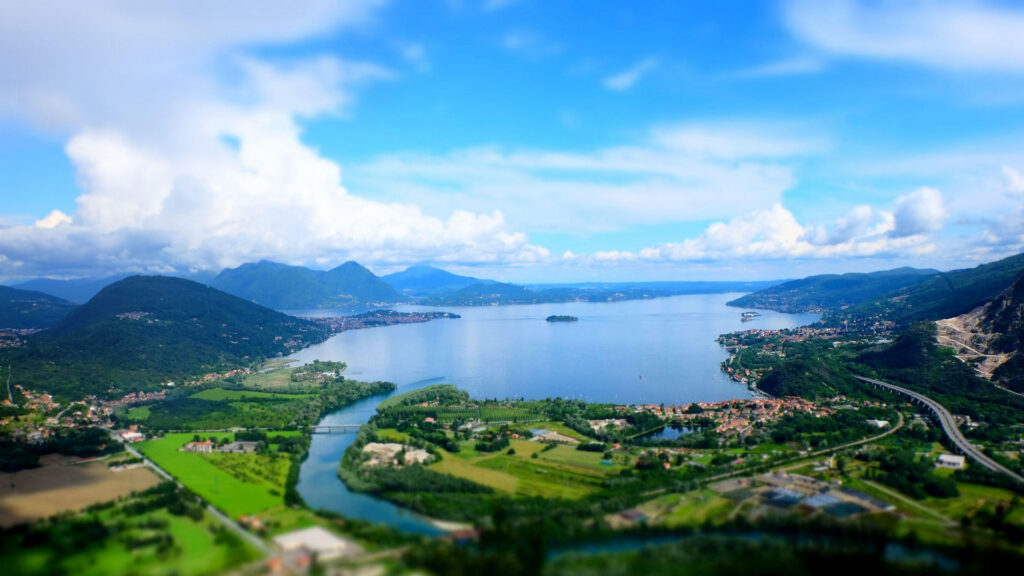 Blick auf den malerischen Lago Maggiore mit grünen Hügeln und Dörfern, die sich entlang des Ufers erstrecken.