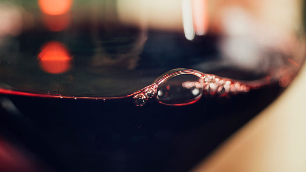Nahaufnahme eines Weinglases, in dem sich Rotwein mit feinen Bläschen an der Oberfläche befindet, zeigt die Leidenschaft zum Wein.