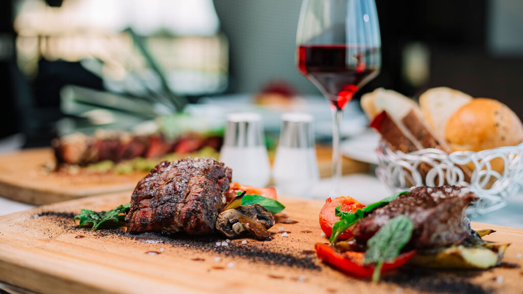 Ein Gourmet-Steakgericht mit Gemüse und einem Glas Rotwein auf einem Holztisch.