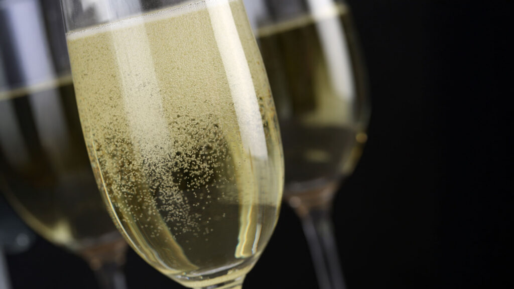 Nahaufnahme von zwei Sektgläsern mit perlendem Schaumwein vor schwarzem Hintergrund.