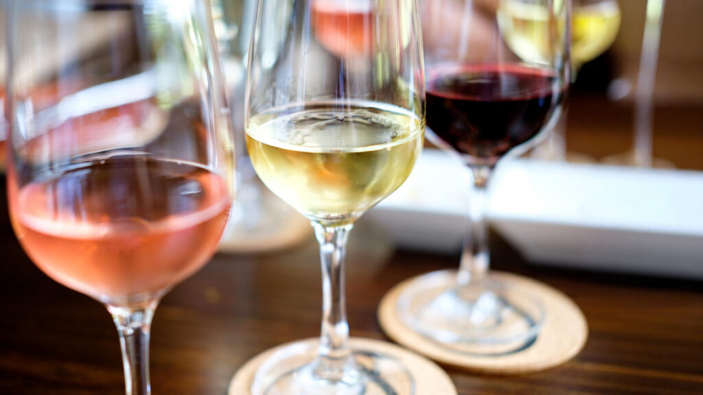 Drei Weingläser mit Roséwein, Weisswein und Rotwein auf Holzuntersetzern auf einem Holztisch.