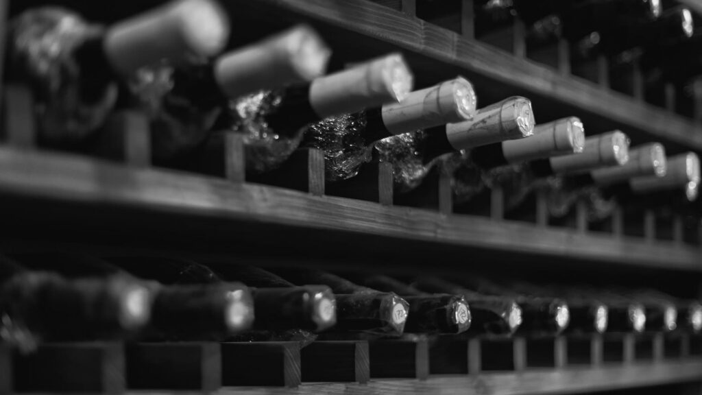 Mehrere Weinflaschen liegen horizontal in einem Holzregal zur Flaschenreifung, Korken sind sichtbar.