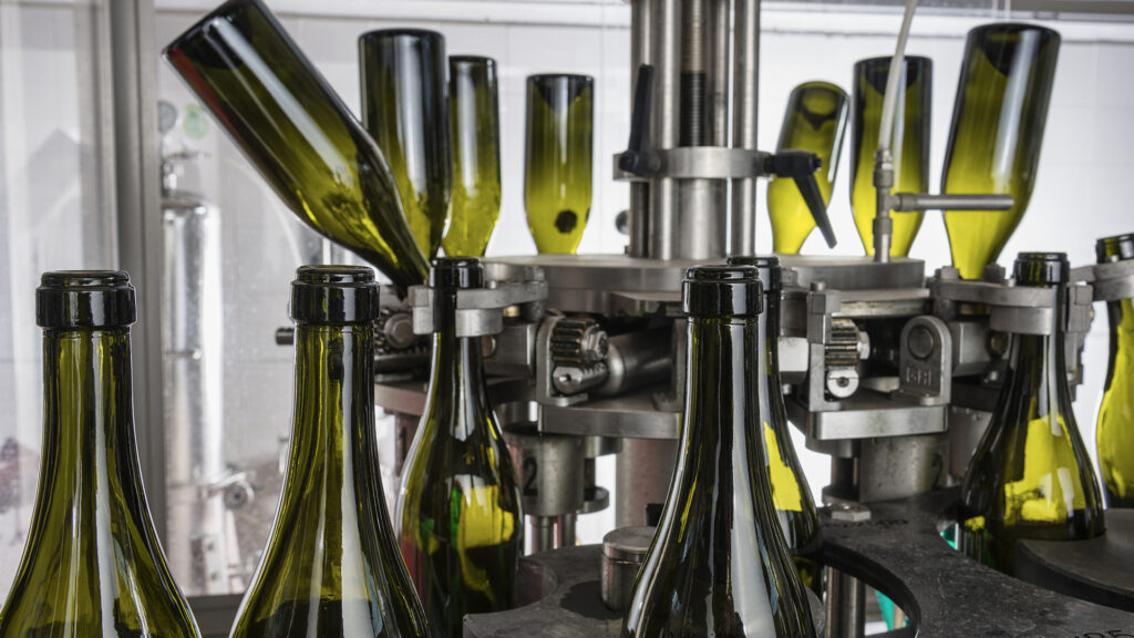 Grüne Weinflaschen stehen kopfüber und aufrecht in einer Abfüllanlage aus Metall.