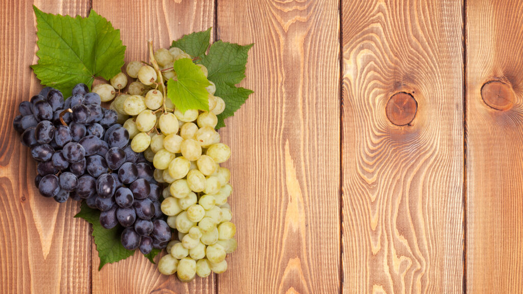 Zwei Trauben, eine dunkel und eine hell, mit Blättern auf einer Holzoberfläche