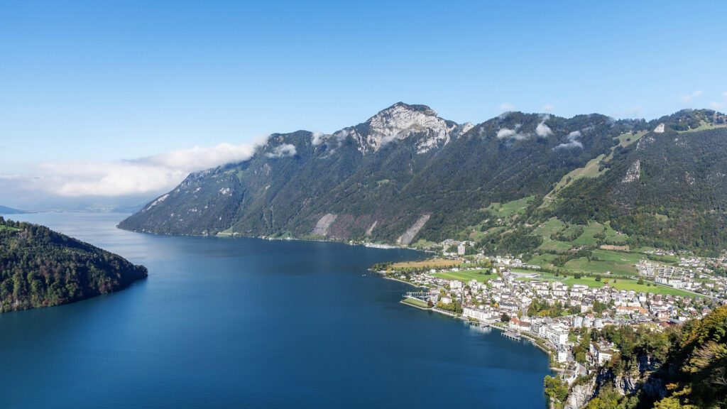 Blick auf den Vierwaldstättersee mit umliegenden Bergen und einer Ortschaft am Ufer