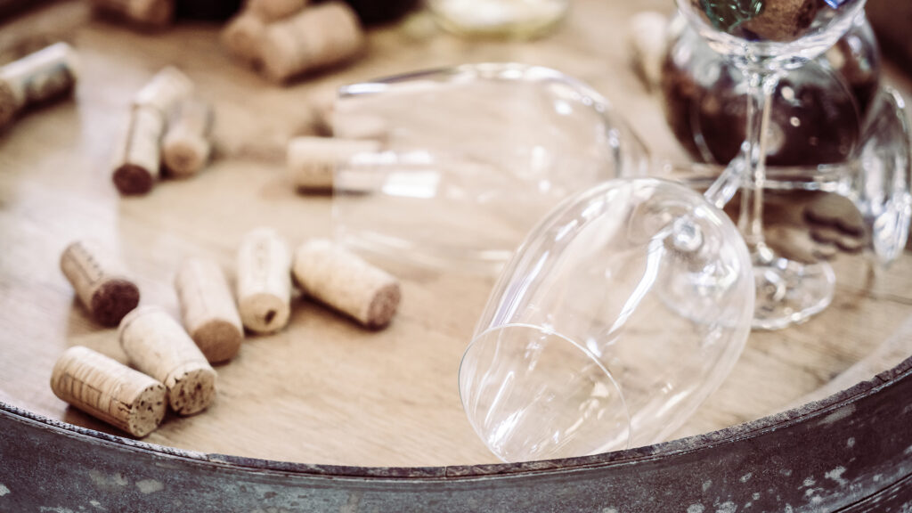Weingläser und zahlreiche Korken liegen auf einem runden Holztisch mit Metallrand.