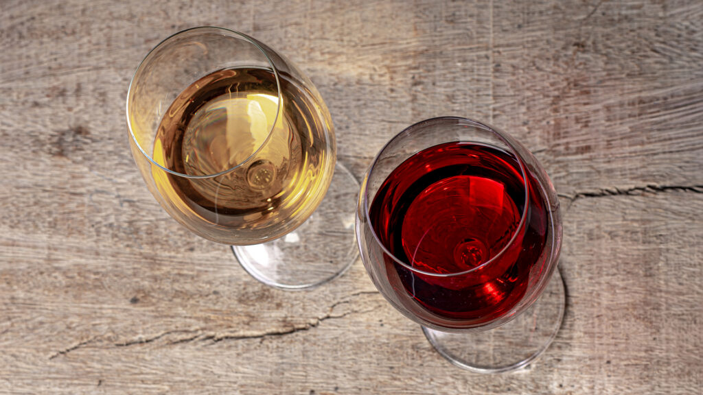 Zwei Weingläser mit Weißwein und Rotwein auf einer Holzoberfläche