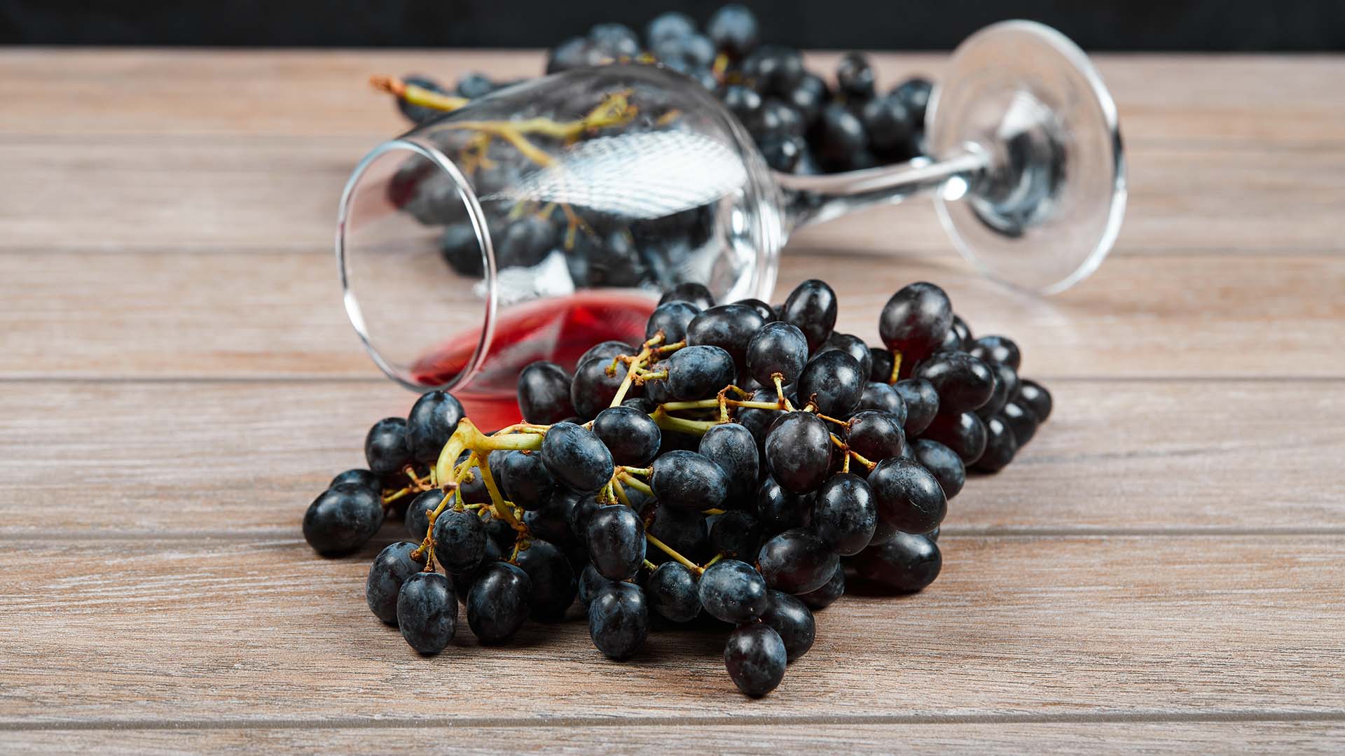 Auf einem Holztisch liegen Sangiovese-Trauben, dazwischen liegt ein Glas mit etwas Rotwein gefüllt